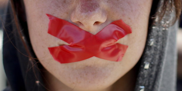 eine Frau hat sich den Mund mit zwei gekreuzten roten Tape zugeklebt