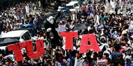Viele Demonstranten auf der Straße, sie halten eine weiße Figur und Schilder mit „TUTAP“ hoch