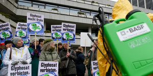 Demonstranten mit Anti-Glyphosat-Schildern, im Vordergrund ein Mann mit Schutzanzug und Sprühflasche