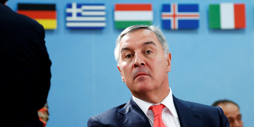 Der montenegrinische Premier Milo Djukanovic sitzt vor einer Wand mit Flaggen