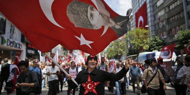 Ein Mann trägt auf einer Demo eine türkische Fahne mit dem Konterfei von Kemal Atatürk durch die Straße