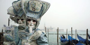 Zwei maskierte VenezianerInnen stehen an einem der Kanäle