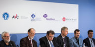 sechs Männer sitzen in einer Reihe, im Hintergrund verschiedene Logos christlicher Organisationen