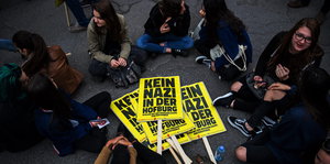 Einige Menschen sitzen um Plakate, auf denen „Kein Nazi in der Hofburg“ steht