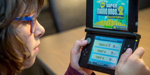 Ein Mädchen mit Brille spielt auf einem Gameboy das Spiel SuperMario