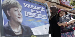 Auf einem Plakat ist Angela Merkel neben dem Satz „Solidarität mit Flüchtlingen“ zu sehen, eine Frau schaut auf das Plakat, daneben ein Kind