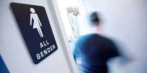An einer WC-Tür hängt ein Schild mit einem Symbol für „All Gender“