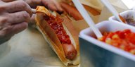 Eine Hand würzt ein Hotdog mit scharfer Sauce