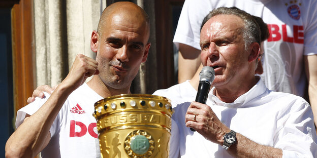 Rumenigge und Guardiola feiern mit DFB-Pokal. Rumenigge hält ein Mikrophon in der Hand