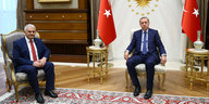 Zwei Männer in Anzügen sitzen in einem Raum, der mit türkischen Fahnen geschmückt ist