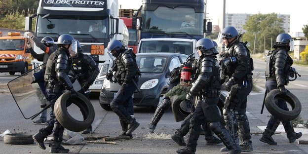 Polizisten in schweren Schutzuniformen tragen Autoreifen weg