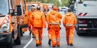 Männer in orangefarbener Kleidung neben Müllautos