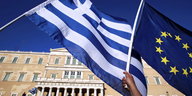 Die griechische Flagge und die EU-Flagge werden vor einem Gebäude geschwenkt