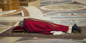 Ein älterer Herr in einem Purpurgewand liegt auf einem Teppich