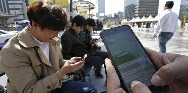 Männer sitzen auf einem öffentlichen Platz und tippen in ihre Smartphones
