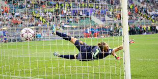 Ein Ball fliegt in ein Fußballtor, eine Torwärtin versucht ihn zu halten