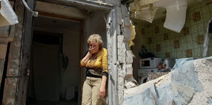 Eine Frau steht im Türrahmen ihres zerstörten Hauses