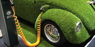 Ein mit Kunstrasen überzogener VW-Käfer an einer Elektrotankstelle