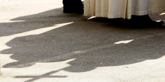 Schatten eines Messdieners, der ein Holzkreuz hält