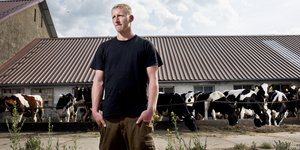 Ein junger Bauer vor einem Stall mit Kühen