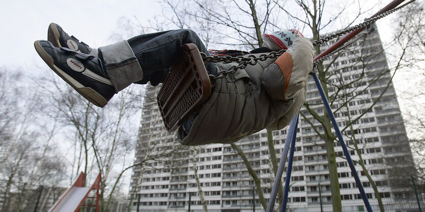 ein Kind auf einer Schaukel, im Hintergrund ein Plattenbau