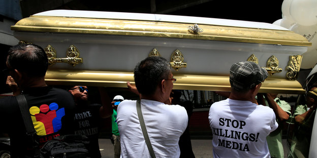 Mehrere Männer tragen einen weiß-goldenen Sarg, einer trägt ein T-Shirt mit der Aufschrift „STOP KILLINGS! MEDIA“