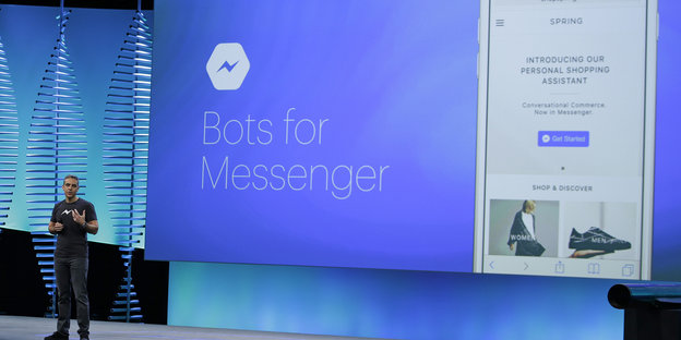 David Marcus steht vor einem blauen digitalen Großdisplay, auf dem „Bots for Messenger“ steht