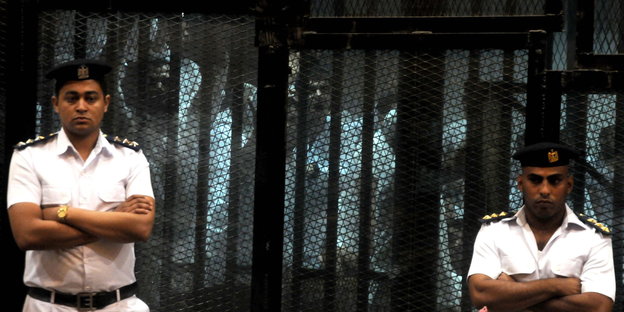 Wachleute vor einem Käfig mit Gefangenen