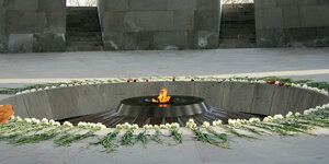 Foto aus einer Gedenkstätte: In der Mitte brennt ein Feuer, drum herum liegen kreisförmig viele Blumen