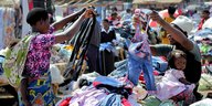Zwei Frauen halten an einem Marktstand Kleidung in die Höhe