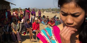 Die Protagonistin Urmila Chaudhary in einem nepalesischen Dorf, im Hintergrund sitzen DorfbewohnerInnen.