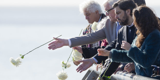Frank-Walter Steinmeier und andere Menschen werfen weiße Rosen