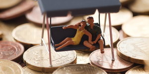 Ein Spielzeugpaar sitzt in einer Hollywoodschaukel, die auf Münzen steht