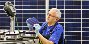 Ein Mann im Blaumann arbeitet in einer Fabrik mit Solarzellen