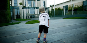 Ein kleiner Junge steht mit dem Deutschlandtrikot vor dem Bundeskanzleramt.