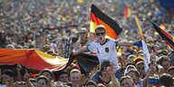 Fußballsfans halten viele Deutschlandflaggen hoch, tragen Sonnenbrillen und gröhlen