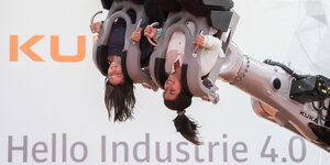 Zwei Frauen in an einem Roboterarm befestigten Sitzen - mit dem Kopf nach unten