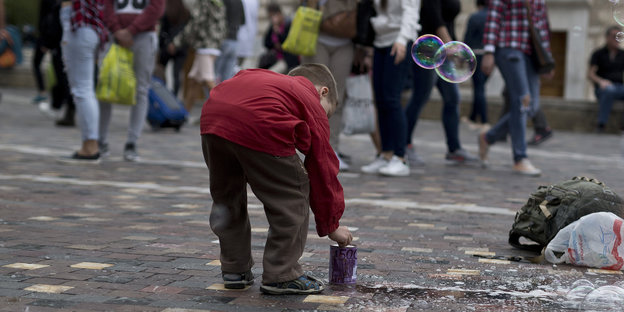 Ein Junge legt Geld in ein Behältnis auf einem Platz in Athen