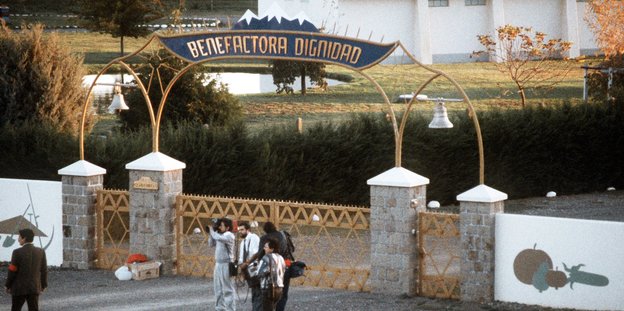 Menschen vor einem Tor, darüber der Schriftzug "Benefactoria Dignidad"