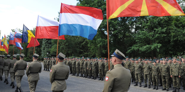 Männer in Uniform laufen in einer Reihe und halten Flaggen verschiedener Nationen
