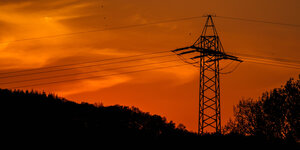 Ein Strommast gegen einen orange gefärbten Abendhimmel