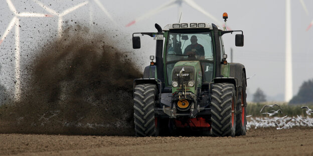 Ein Bauer wirbelt mächtig Erde in die Luft, während er mit seinem Traktor ein Feld bestellt
