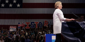 Hillary Clinton steht am Podium, Unstersützer halten Poster in die Höhe mit der Aufschrift "History"