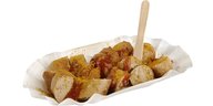 Eine fachgerecht zerstückelte Currywurst in einer Pappschale mit Pommesgabel
