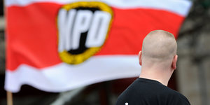 Ein Mann mit Glatze steht vor einer NPD-Fahne
