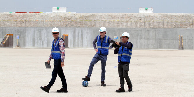 Drei Männer mit Bauarbeiterhelmen stehen auf einer leeren Baustelle