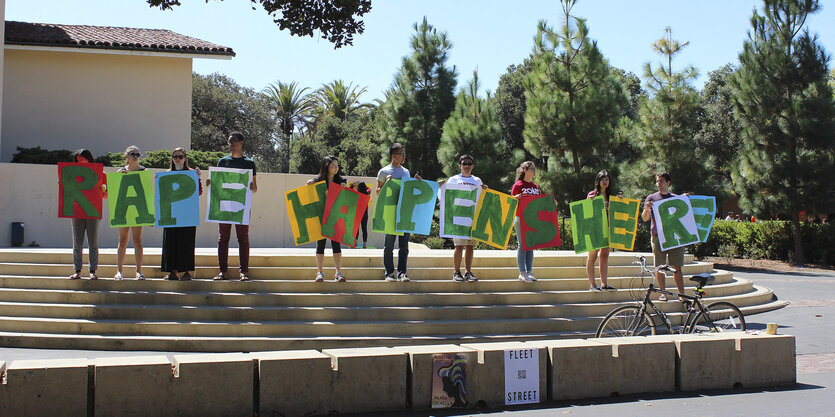 Student_innen halten Buchstaben hoch, die den Satz „Rape happens here“ ergeben