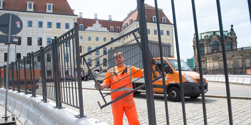 Mann in orangenem Overall montiert Zaun vor Gebäude in Dresden