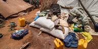 Junge aus Mosambik liegt neben Wasserkanistern auf Lebensmittelsäcken in einem Flüchtlingscamp in Malawi
