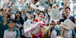 Chinesische Studenten jubeln und werfen Papiere in die Luft